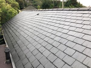 A slate shingle roof featuring a prominent chimney against a clear sky backdrop.