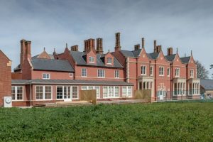 Side view of the red manor house and a glass-enclosed conservatory addition.
