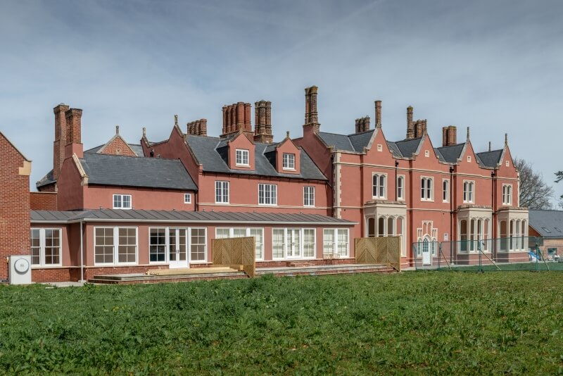 Side view of the red manor house and a glass-enclosed conservatory addition.