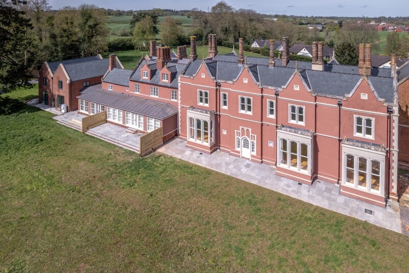 Aerial view of the terracotta red manor house and its grounds, showing a long glass conservatory.