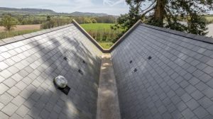 View down a roof valley with slate tiles and countryside in the background.