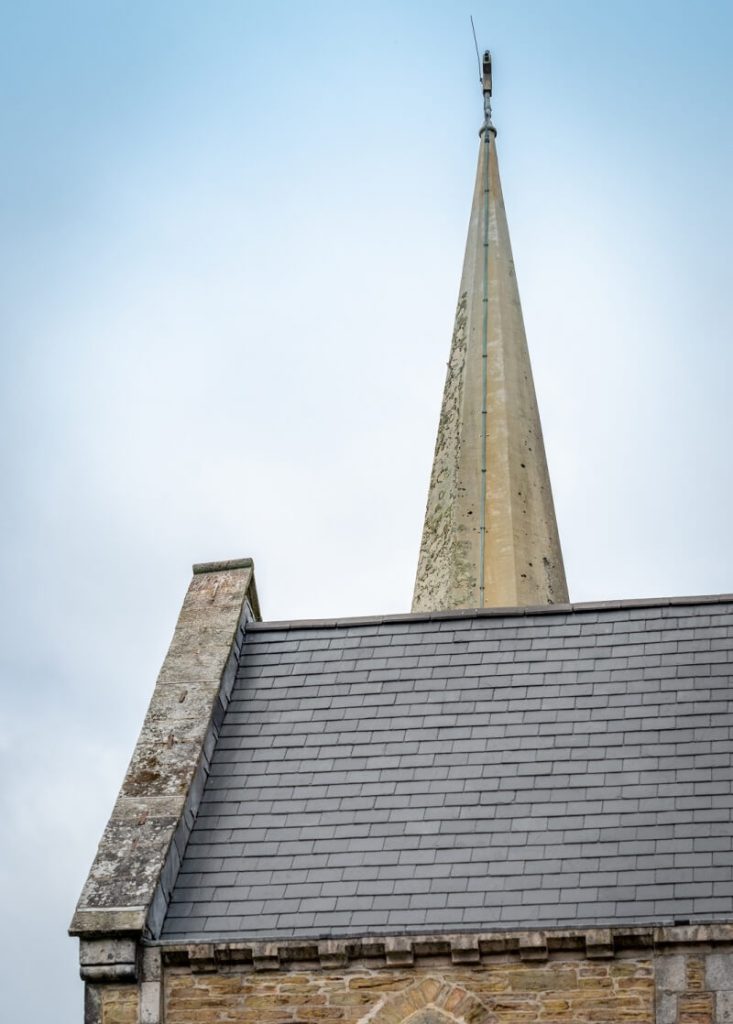 Close-up of a tall, narrow stone spire rising from the dark slate roof of St Paul's Church.