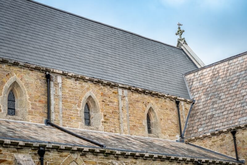 Exterior view of a sandstone wall with Gothic arched windows and the slate roof of St Paul's Church.