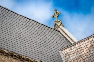 Detail of a Celtic cross finial and slate roof on St Paul's Church against a blue sky.