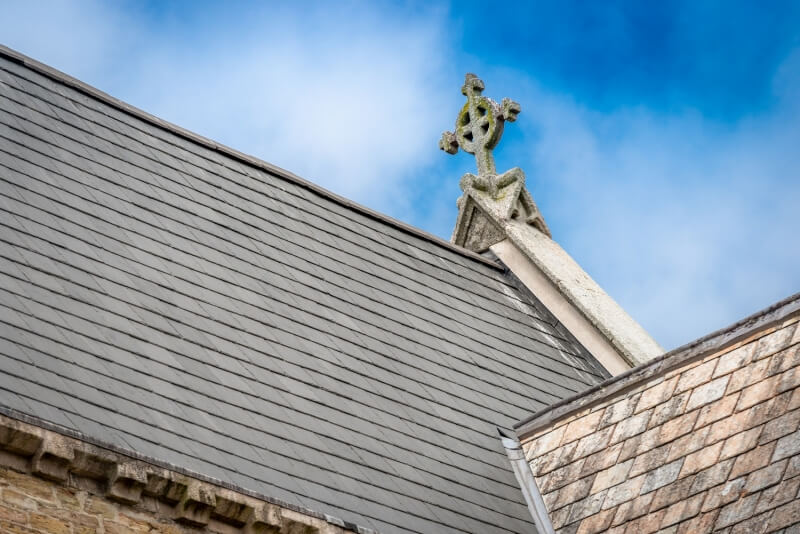 Detail of a Celtic cross finial and slate roof on St Paul's Church against a blue sky.