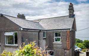 Close-up of a roof valley and gable end featuring grey tones of SSQ Riverstone Ultra natural slate against pebble-dash walls.