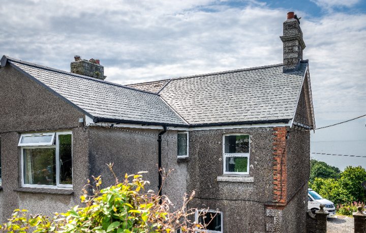 Close-up of a roof valley and gable end featuring grey tones of SSQ Riverstone Ultra natural slate against pebble-dash walls.