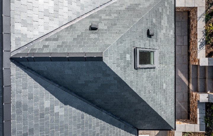 A top-down aerial shot highlighting the precision of the slate installation on a roof hip and valley, featuring a built-in skylight.