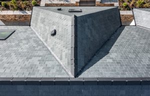 An overhead perspective of the multi-faceted slate roof, showing the clean lines of the ridge tiles and integrated roof vents against the landscaped garden.