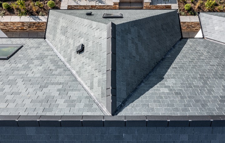 An overhead perspective of the multi-faceted slate roof, showing the clean lines of the ridge tiles and integrated roof vents against the landscaped garden.