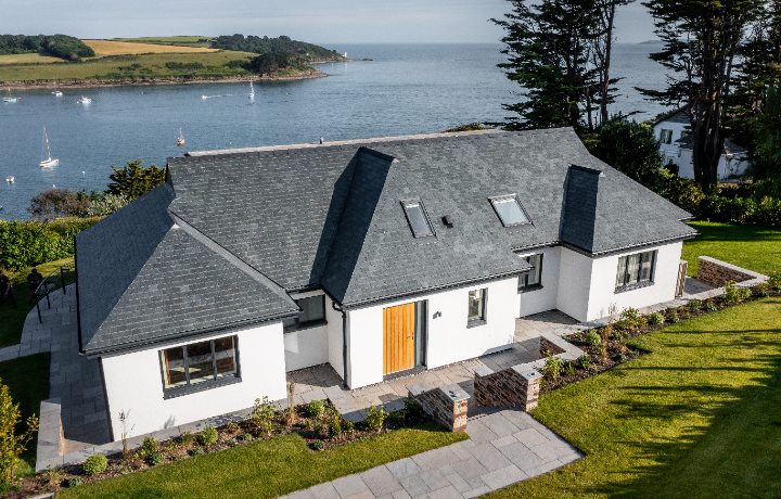 An elevated wide shot of the entire coastal residence, showing how the grey natural slate roof complements the white masonry and the surrounding ocean landscape.