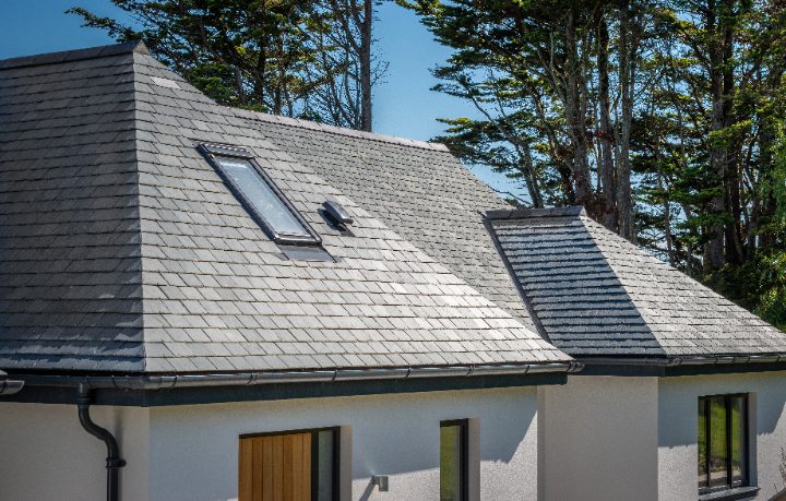 A close-up architectural shot of the roof’s steep pitch and slate texture, featuring a large skylight and sleek black guttering.