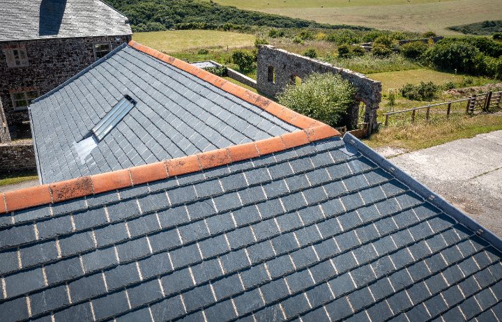 A high-angle close-up highlighting the uniform texture of the grey Riverstone slates and the clean lines of the terracotta ridge cap on the barn roof.