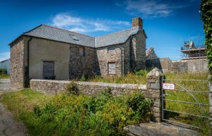 A ground-level perspective of the historic Berry Barns cottage, showing the contrast between the weathered stone walls and the pristine, heritage-sensitive slate roof.