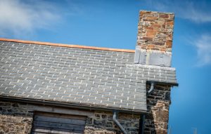 A detailed shot of the stone chimney stack integrated with the new slate roofing, featuring lead flashing and grey guttering.
