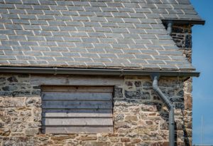 A close-up focus on the eaves of the cottage, showcasing the thick, durable profile of the Riverstone slates and the traditional stone masonry.