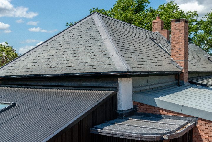 Detailed view showing the clean transition between the restored natural slate roof, flat seam roof, and corrugated sections.